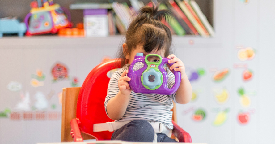 Baby-girl-sitting-on-the-high-chair-and-looking-through-toy-camera