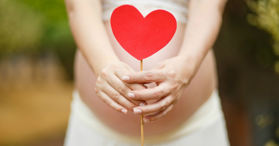 pregnant woman holding a paper red heart in front of her