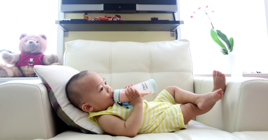 baby drinking milk and lying on the white sofa